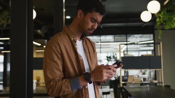 Mixed race businessman standing using a smartphone in a modern office