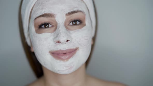 Cute Girl with Cosmetic Mask on Face Looks with Smile Into Camera on Background