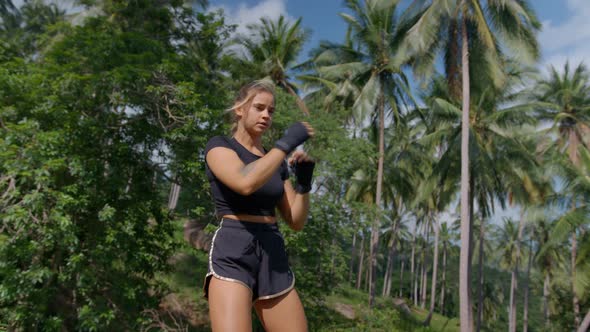 Sporty Girl in Black Shorts Practicing Boxing with Hands in Fingerless Gloves Among Tropical Palms