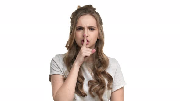 Portrait of Serious Brunette Woman with Long Hair Looking at Camera Holding Index Finger on Lips and