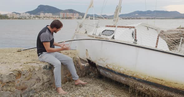 The Man Sits in Despair Near His Yacht Broken After a Storm.