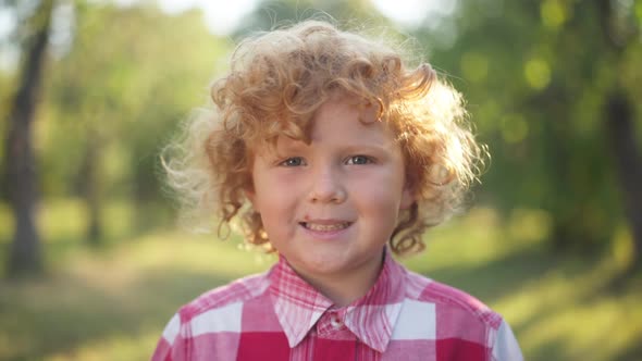 Closeup Portrait of Cheerful Redhead Little Boy with Curly Hair Looking at Camera Smiling Standing