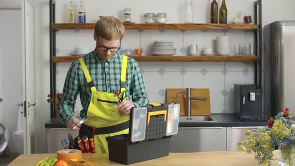 Young Plumber Taking Necessary Tools From Box in Kitchen