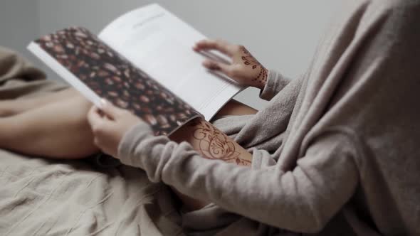 Young Woman Is Sitting on Bed and Reading Book in Evening, Detail Shot