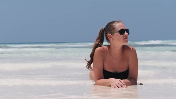 Young Woman in Black Bikini Tans on a Paradise White Sandy Beach Lies By Ocean