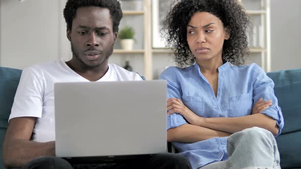 African Man Using Laptop While Angry Girlfriend Sitting Aside