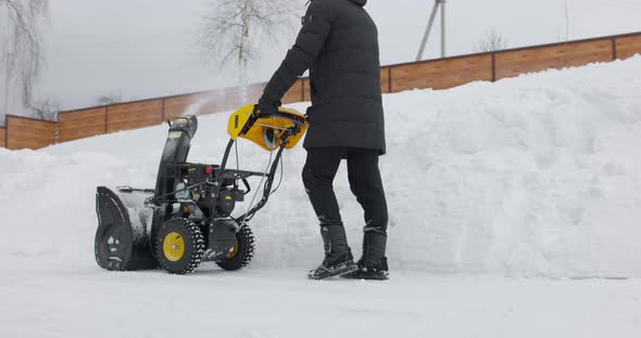 Man Removing Snow with Mechanical Snowplough at House Courtyard