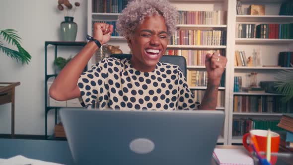 Excited African Woman Winner Looks at Laptop Celebrates Success at Home Office