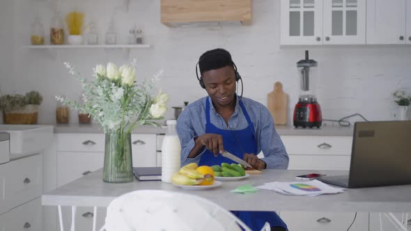 Young Cheerful Man Cooking Healthful Salad in Kitchen Talking at Laptop Virtual Conference