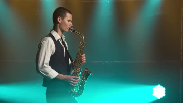 A Young Retro Stylish Guy Plays on the Golden Shiny Saxophone in the Turquoise Spotlights on Stage