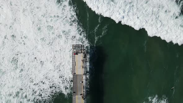 Large waves breaking under a concrete walking platform built out to the ocean. High drone view looki