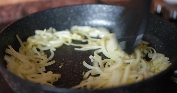 The Cook Stirs the Fried Onions in the Pan with a Black Spatula