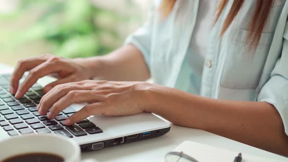 Young woman with cup of coffee sitting at living room and working on laptop at home