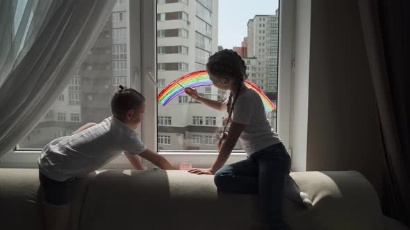 Children at Home, Boy and a Girl Draw a Rainbow on the Window Glass, Quarantine, Drawing