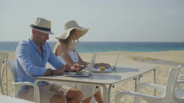 Couple Using Laptops Together on Beach