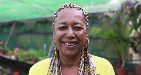 African woman working inside nursery greenhouse while smiling on camera - Green market concept