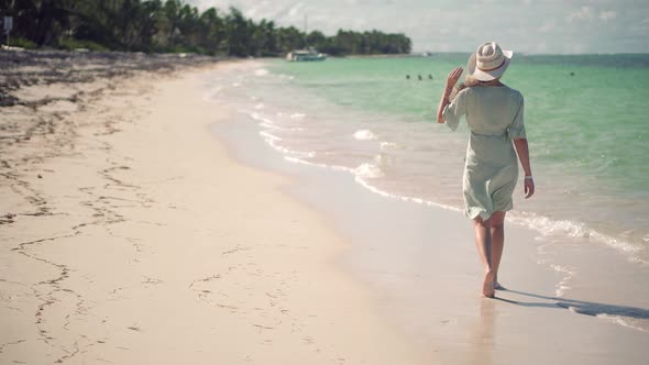 Woman Relaxing On Bahamas Flowing Dress Blowing In Wind.Woman In Hat Walks Along Beach On Caribbean