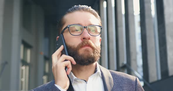 Bearded Businessman in Glasses which Talking on Mobile with Business Partner Outdoors