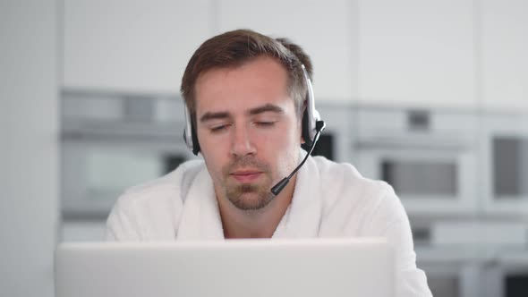 Young Man Wearing Headset Speaking and Watching Business Webinar Sitting in Kitchen