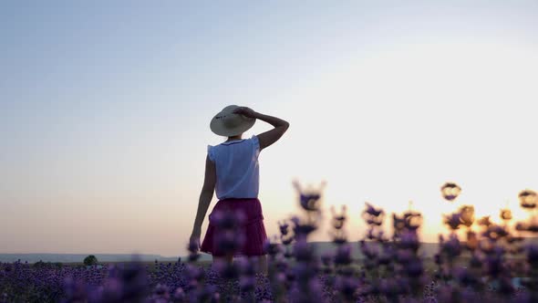 Woman in a Short Purple Dress and a Hat Stands on a Lavender Field