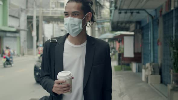 Young Asian businessman wearing a mask holding coffee cup during walking in the street.