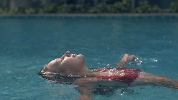 Young Lady Relaxes Swimming on Back in Clear Blue Pool