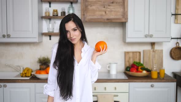 Young Brunette Woman Holding Oranges On Kitchen And Smiling