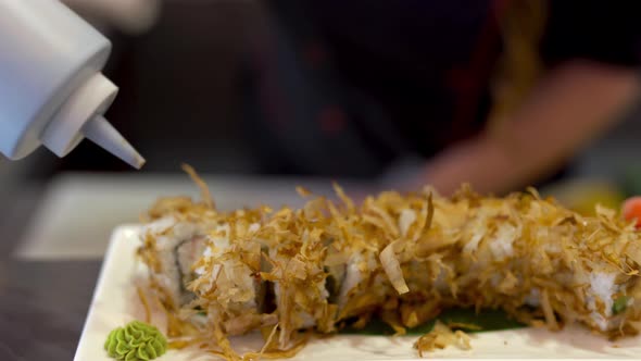 On the foreground we see a plate with sushi. On the background chef is doing some preparations and t