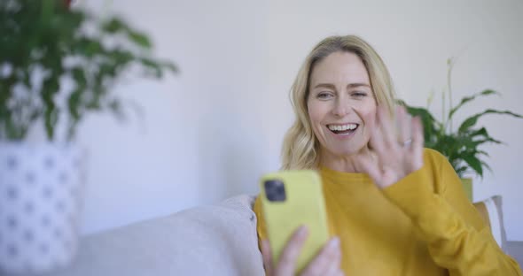 Mature woman sitting on sofa making video call on smartphone