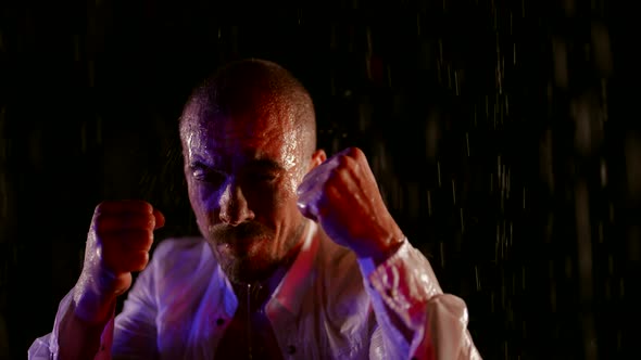 a Man in an Unbuttoned White Shirt Raises Fists and Stands in the Streams of Water on a Dark