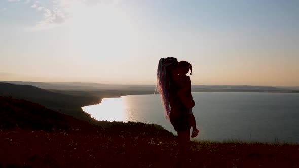 A Girl with Her Little Daughter Is Enjoying the Sunset on Shore of Mountain Lake.