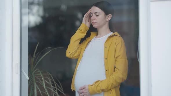 Anxious Worried Pregnant Woman Touching Forehead Standing Indoors Behind Glass Door