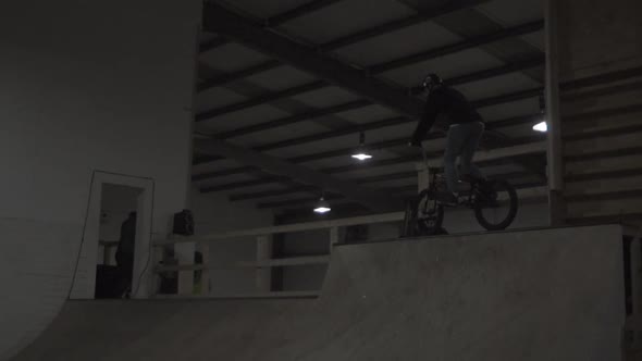 A boy rides a BMX bike on an indoor skate park half pipe ramp.