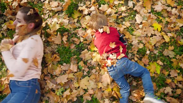 Video of Smiling and Laughing Mother with Little Son Rolling on Grass Covered with Yellow Fallen