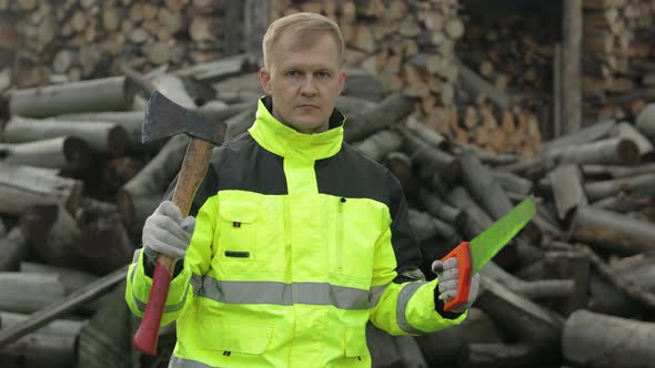 Lumberjack in Reflective Jacket. Man Woodcutter Holds Small Axe and Saw on His Hands. Firewood