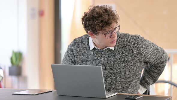 Young Man with Back Pain Using Laptop at Work 