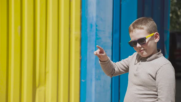 Positive Boy in Glasses Near Blueyellow Wall Writes His Fingers in the Air