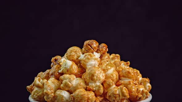 Coffee taste popcorns rotating into the bowl on black background close up. Caramel popcorn. Health