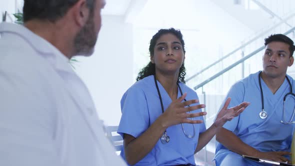 Asian female doctor sitting and discussing with diverse male colleagues at hospital staff meeting