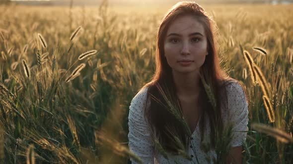 Lonely Calm Teenage Girl Is Sitting in Ears of Wheat in Summer Sunset Time