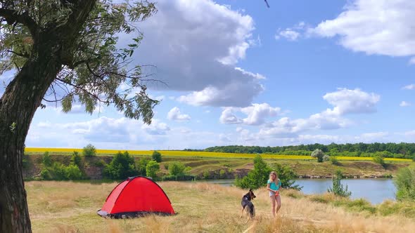 Girl Playing with a Dog Near a Tent on a Beautiful Hill Near River