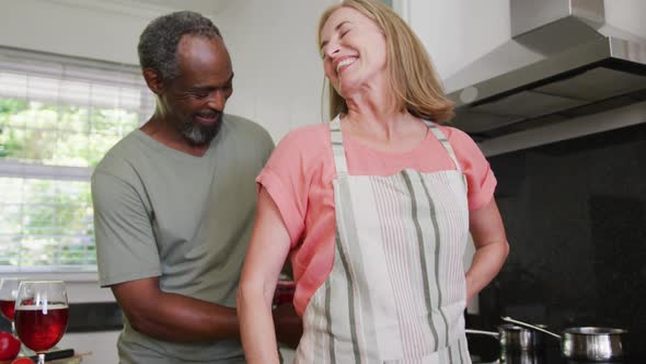 Diverse senior couple putting on apron before preparing food in kitchen