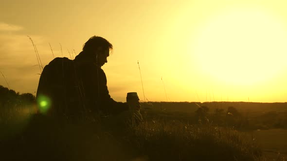 Lonely Traveler Sitting on Top of a Hill Drinking Coffee in Thermos. Tourist Drinks Hot Tea and