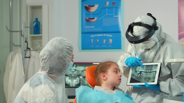 Dentist in Protective Equipment Showing on Tablet Dental Xray of Child