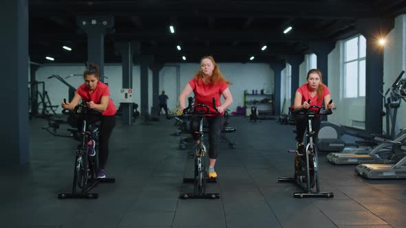 Athletic Women Group Riding on Spinning Stationary Bike Training Routine in Gym Weight Loss Indoors