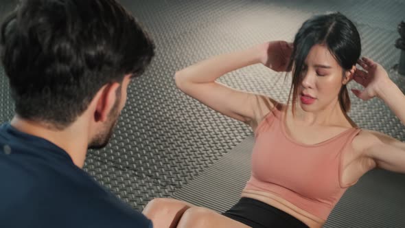 Asian young beautiful sport woman training sit up in gym with trainer holding legs in fitness club.