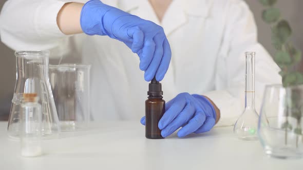 Woman pharmacist opening pipette dropper with drop of natural oil.