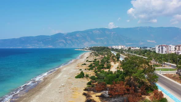 aerial drone panning low across a highway towards a white sandy tropical beach with the Mediterranea