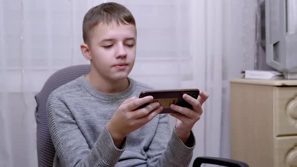 Child Sits in a Chair Holds a Smartphone in Hands Reads SMS in Screen