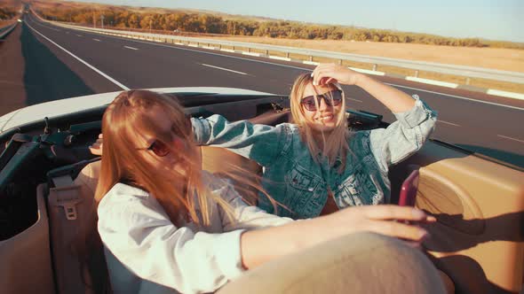 Women in Sunglasses Take Selfies While Posing in a Convertible Happy and Laughing